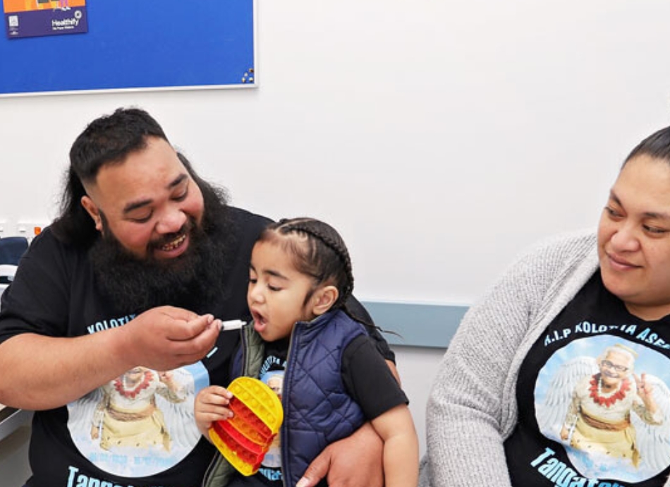 HN 1961 Father giving toddler son medicine with an oral syringe with mother looking on 950x690