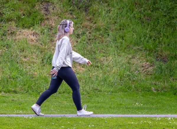 Young woman walking along path wearing headphones