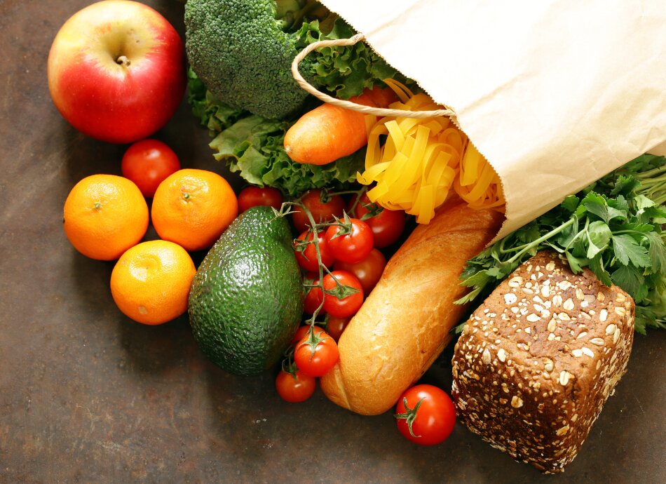 Fresh groceries and bread spill out of brown bag onto table