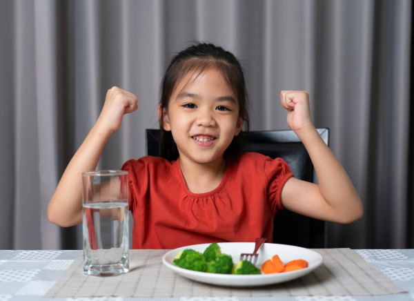 Girl strikes strong pose and eats broccoli and carrots