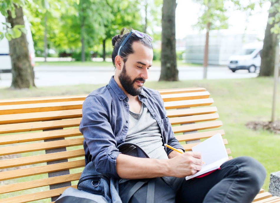 Man sitting on park bench writing notes