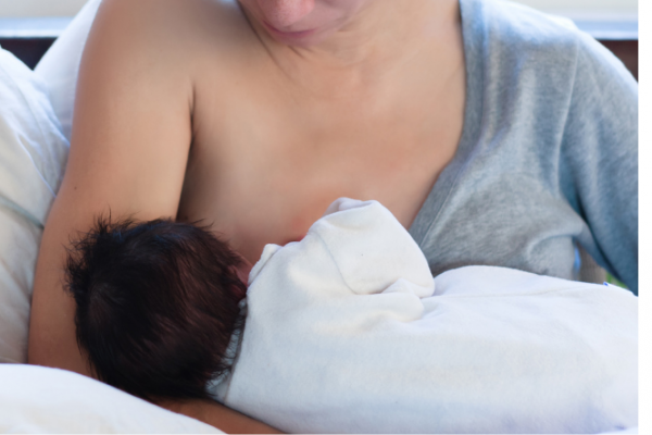 Mother breastfeeds infant lying on a pillow across her lap