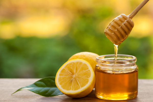 Lemons next to honey being drizzled into a jar